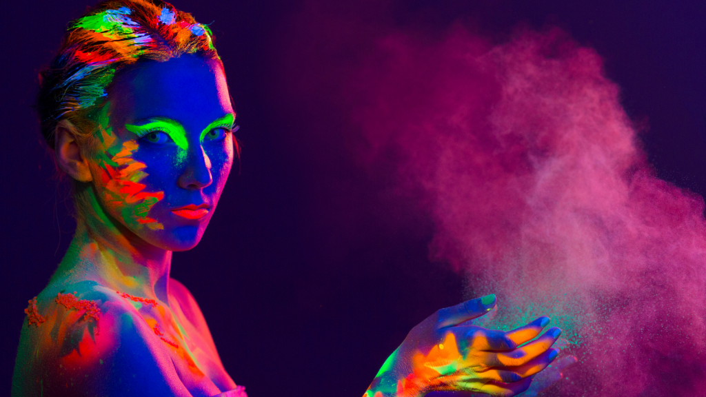 An AFAB person covered in uv paint creating a cloud of glowing pink dust with their hands